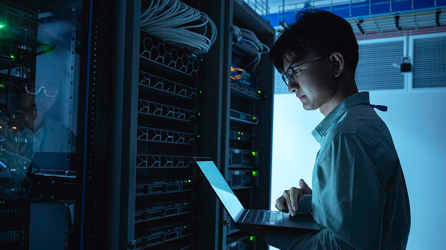 Engineer working on a laptop beside server racks